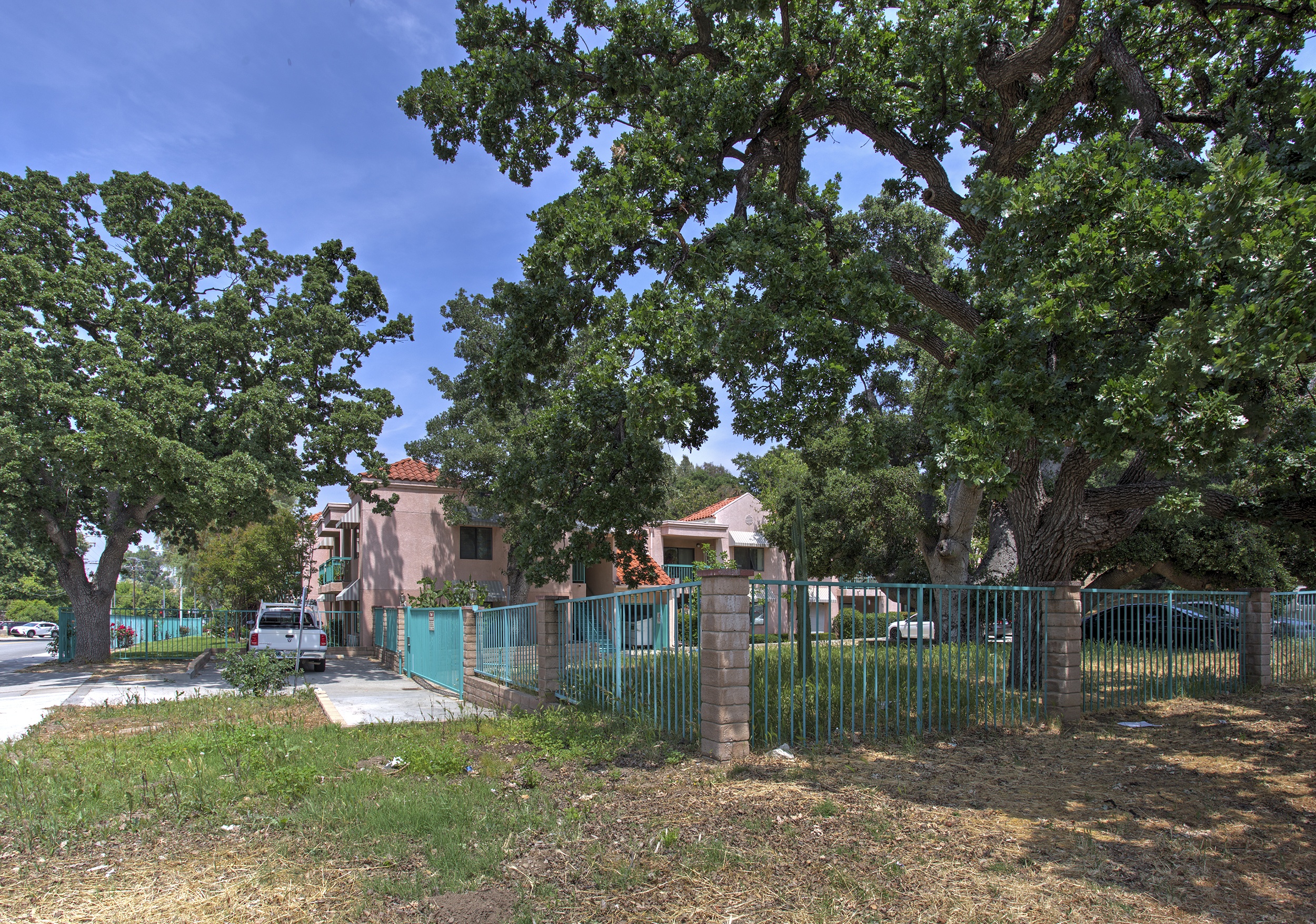 A tree-lined street with a fence and a building in the background.